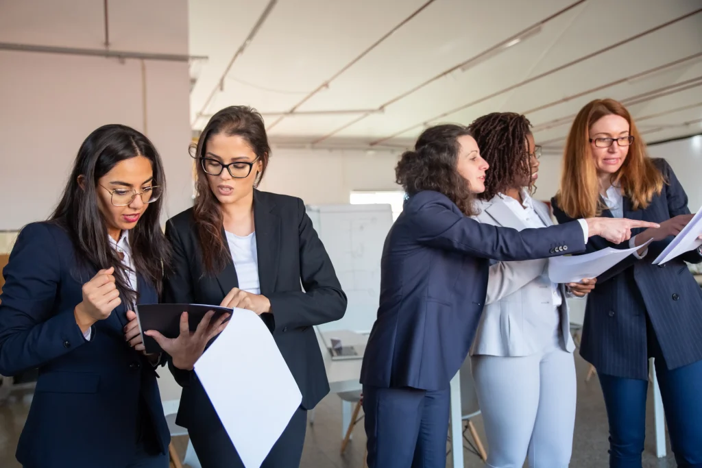 Cinco mujeres profesionales trabajando en equipo y revisando documentos en una oficina, representando el liderazgo femenino en Chile.